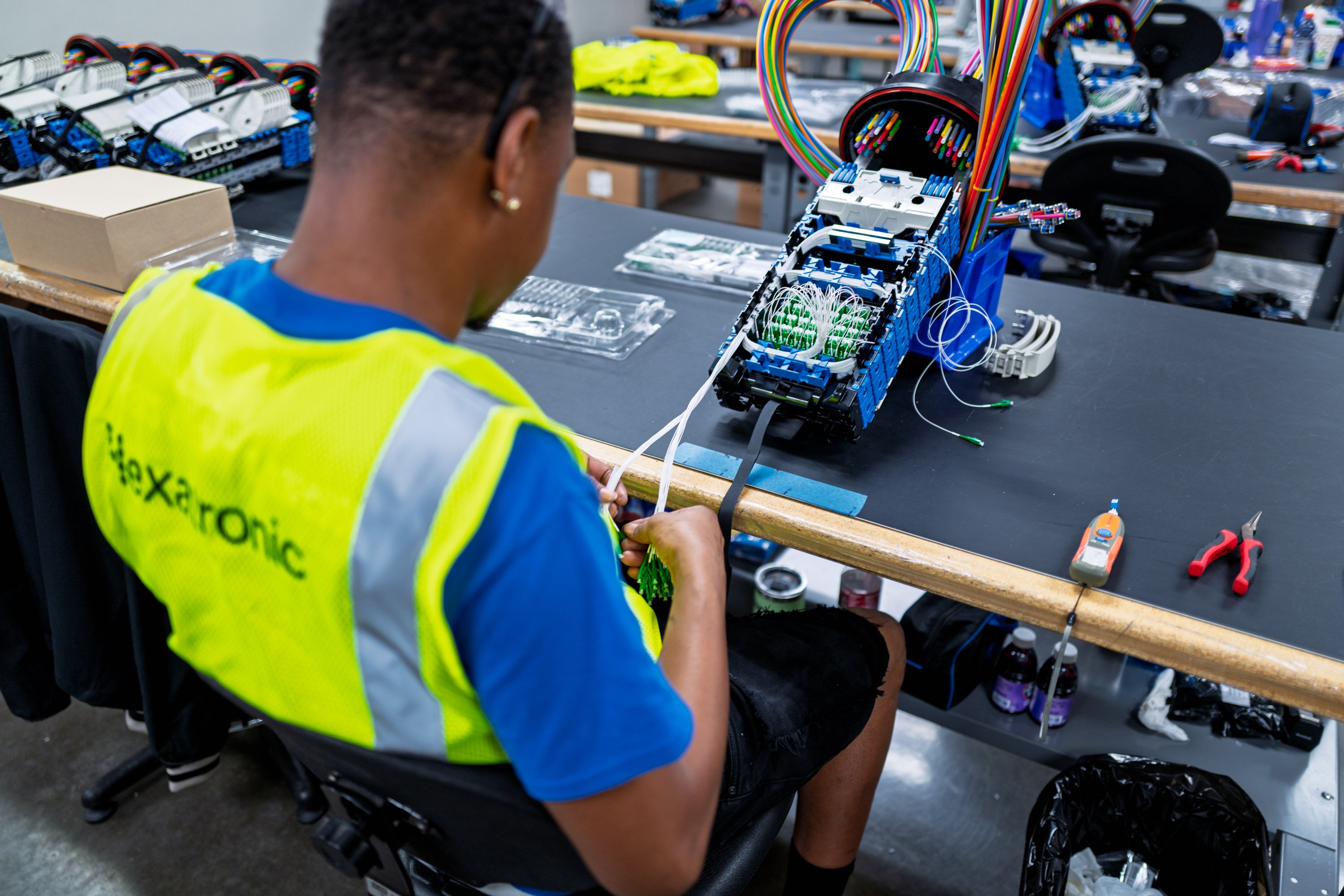Worker in high-visibility vest assembling wiring at workstation.