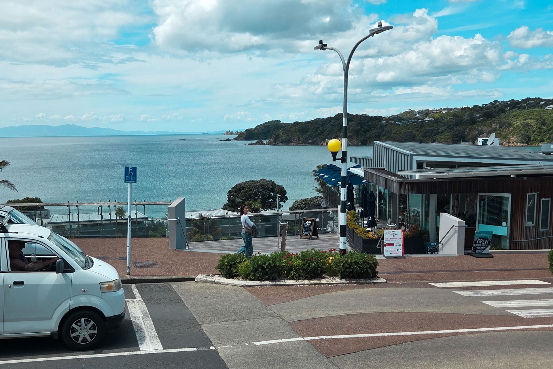 A street with an ocean view and a pedestrian in New Zealand.